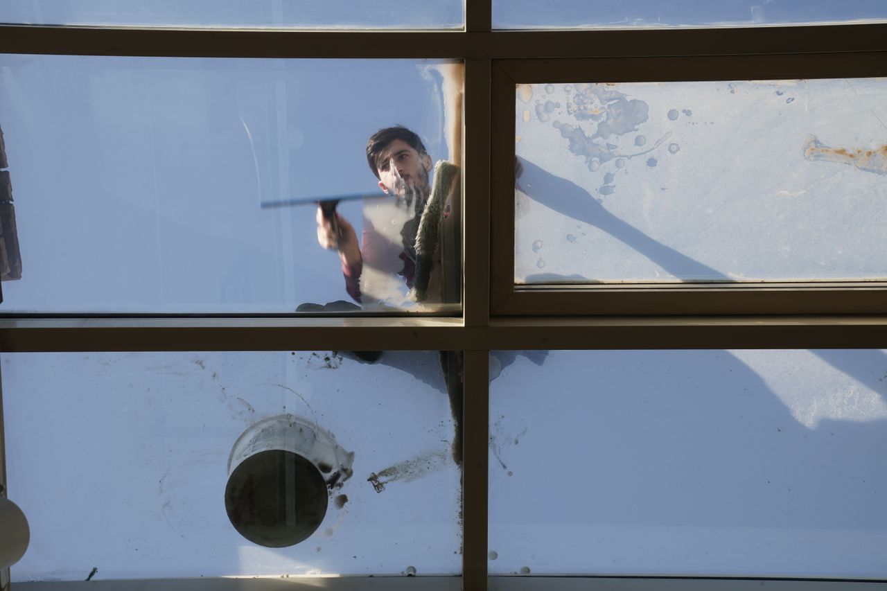 A man cleaning the outside glass roof from above with a tool in daylight.